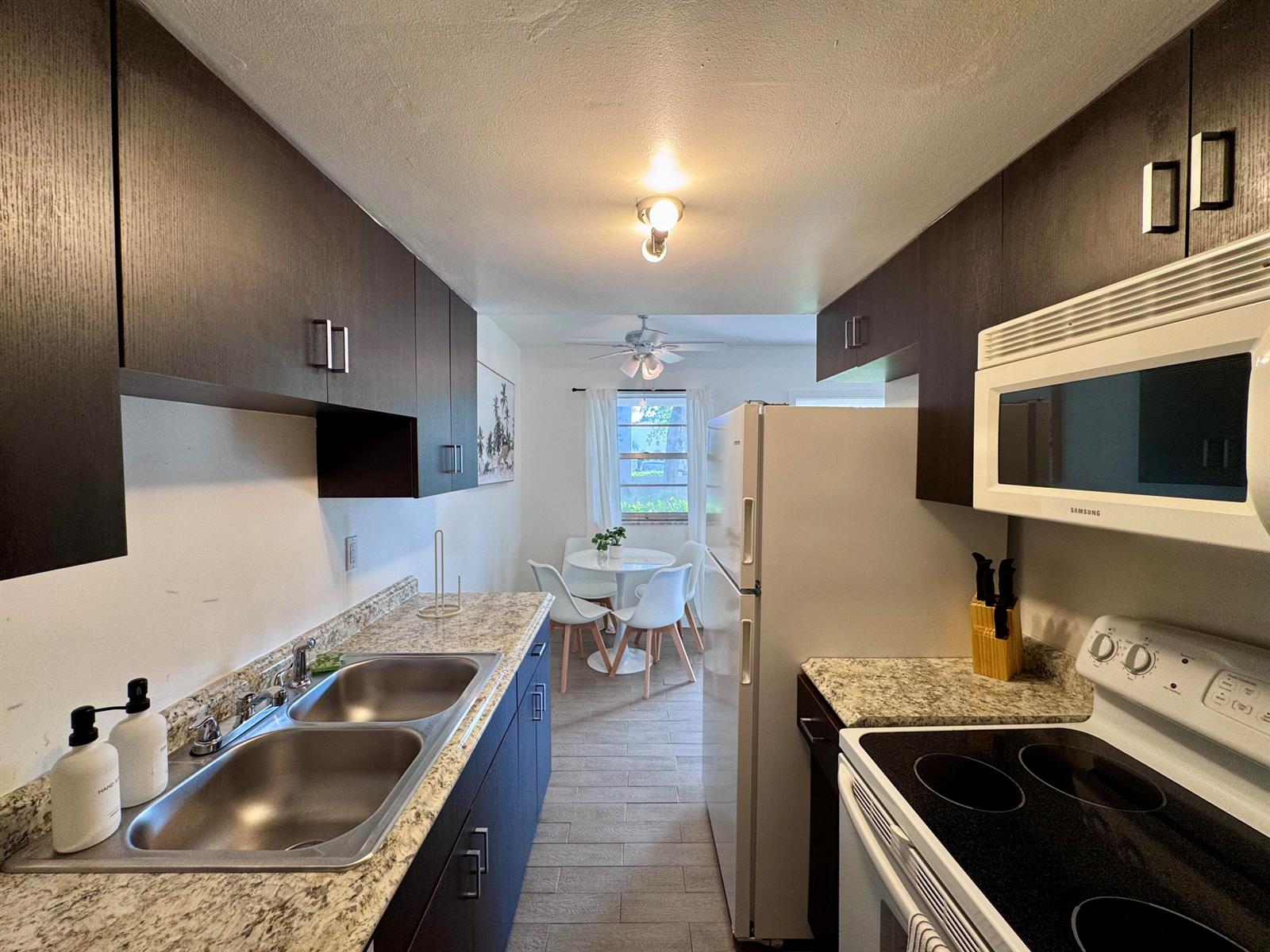 A galley kitchen with dark cabinets, granite countertops, and a dining area in the back — 202 Lucerne Avenue Unit 9, FL 33460, FL