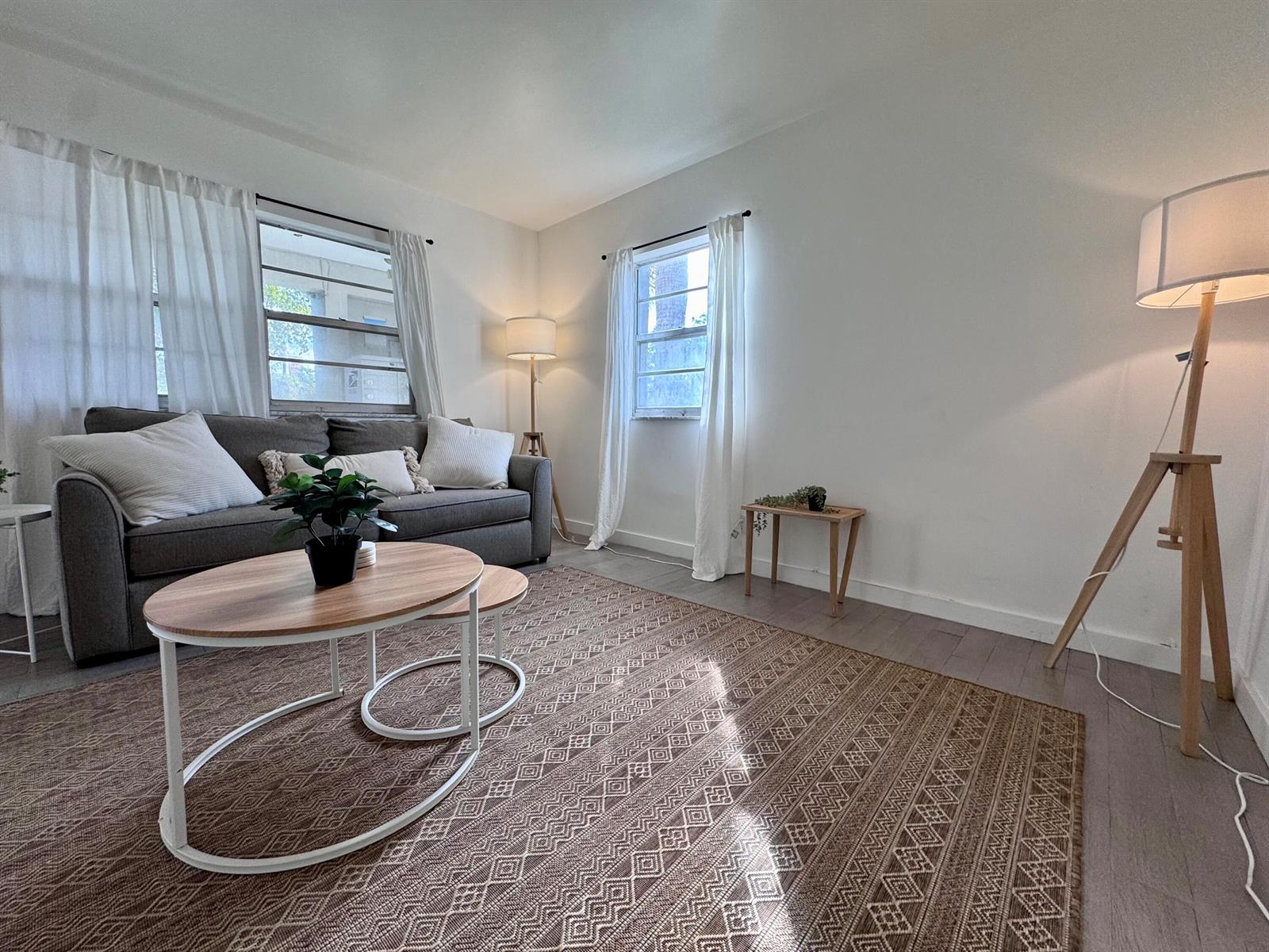 A living room features a grey sofa, nested coffee tables, a patterned rug, and floor lamps — 202 Lucerne Avenue Unit 9, FL 33460, FL