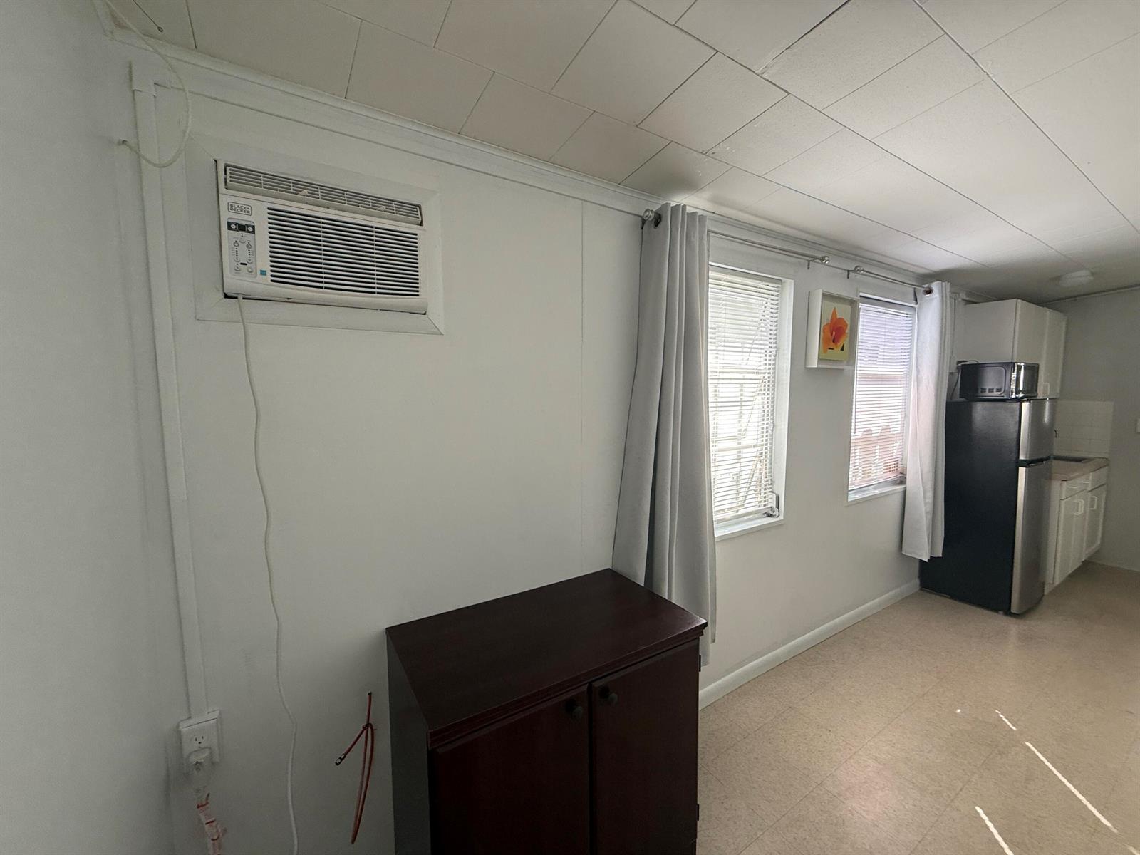 A room with a wall-mounted air conditioner, a dark cabinet, two windows, and a refrigerator — 605 E Coast Avenue # 2, Lantana FL 33462, LANTANA, FL