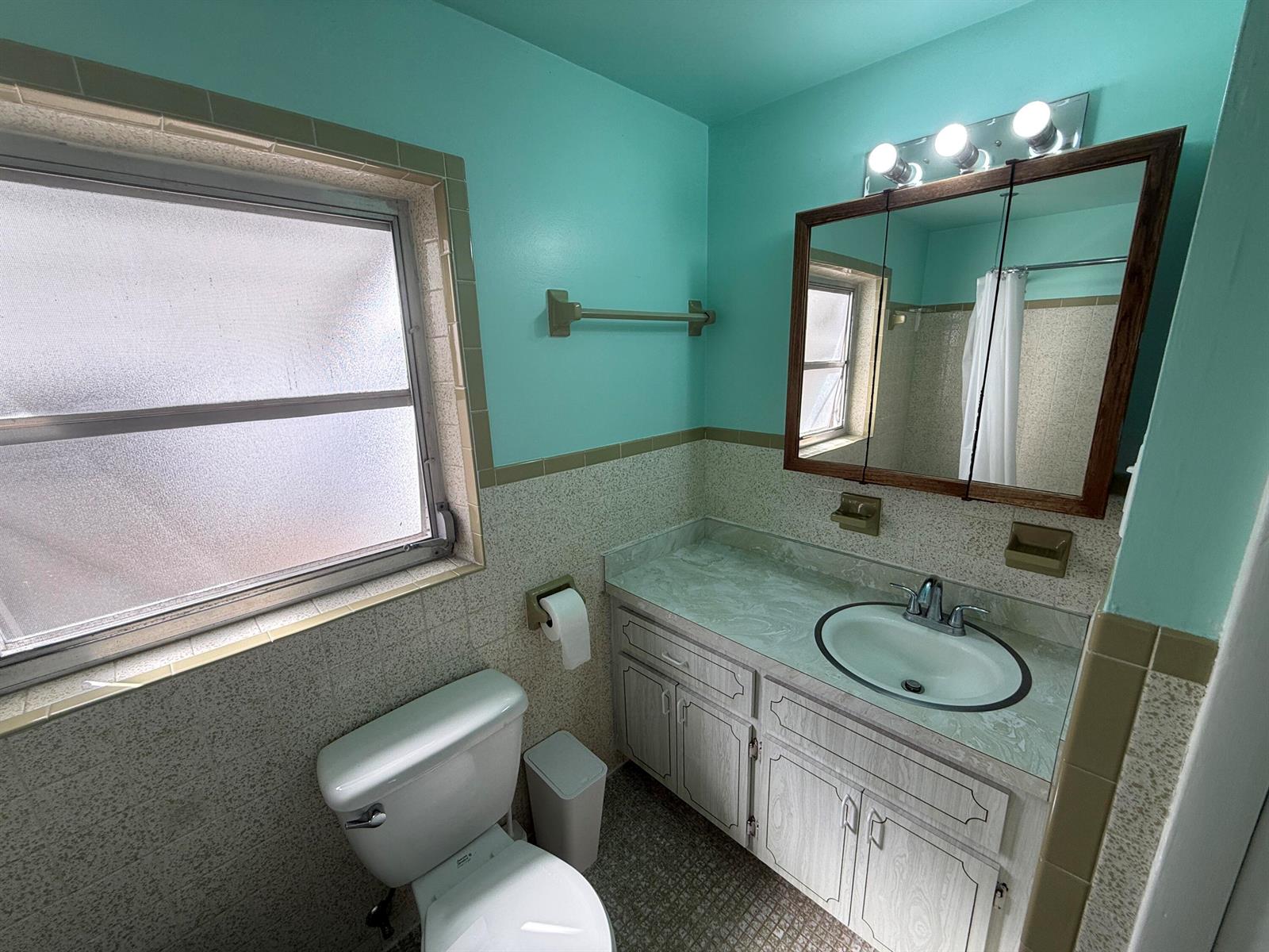 A bathroom features turquoise walls, a vanity with a laminate countertop, and tan tiled wainscoting — 605 E Coast Avenue # 2, Lantana FL 33462, LANTANA, FL