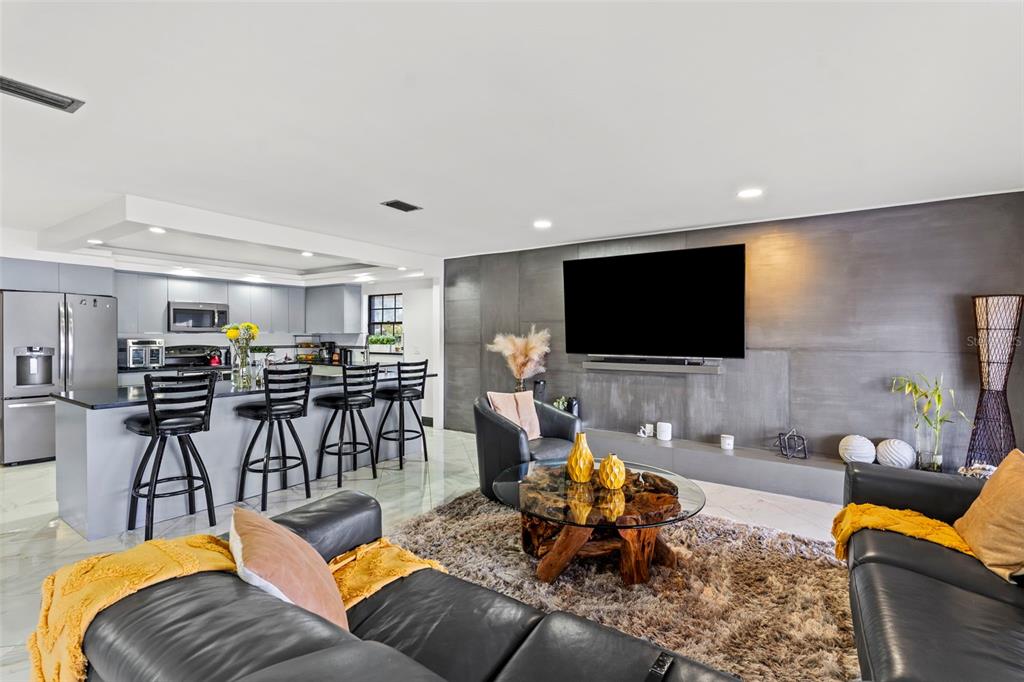 An open-concept living room and kitchen featuring a dark accent wall and leather furniture — 7302 EGYPT LAKE DRIVE, TAMPA, FL