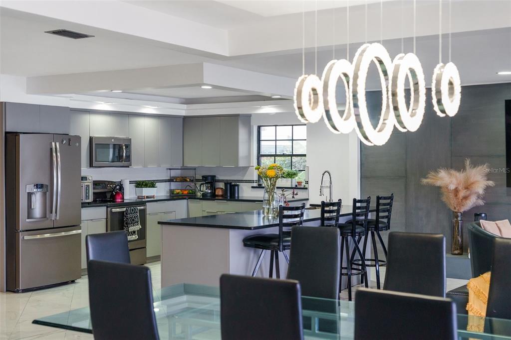 A modern kitchen features gray cabinetry, a black island with bar stools, and a ring chandelier — 7302 EGYPT LAKE DRIVE, TAMPA, FL