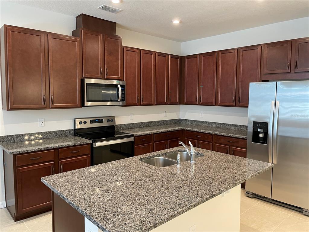 A kitchen features dark wood cabinets, granite countertops, stainless steel appliances, and a central island — 16347 PRAIRIE SCHOOL DRIVE, WINTER GARDEN, FL