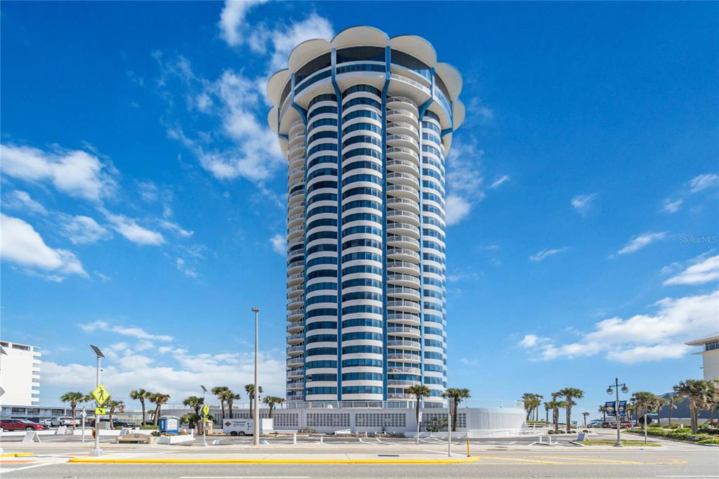 An aerial view shows a tall, cylindrical beachfront tower surrounded by other hotels and parking lots — 2625 SOUTH ATLANTIC AVENUE UNIT 12BSW, DAYTONA BEACH SHORES, FL