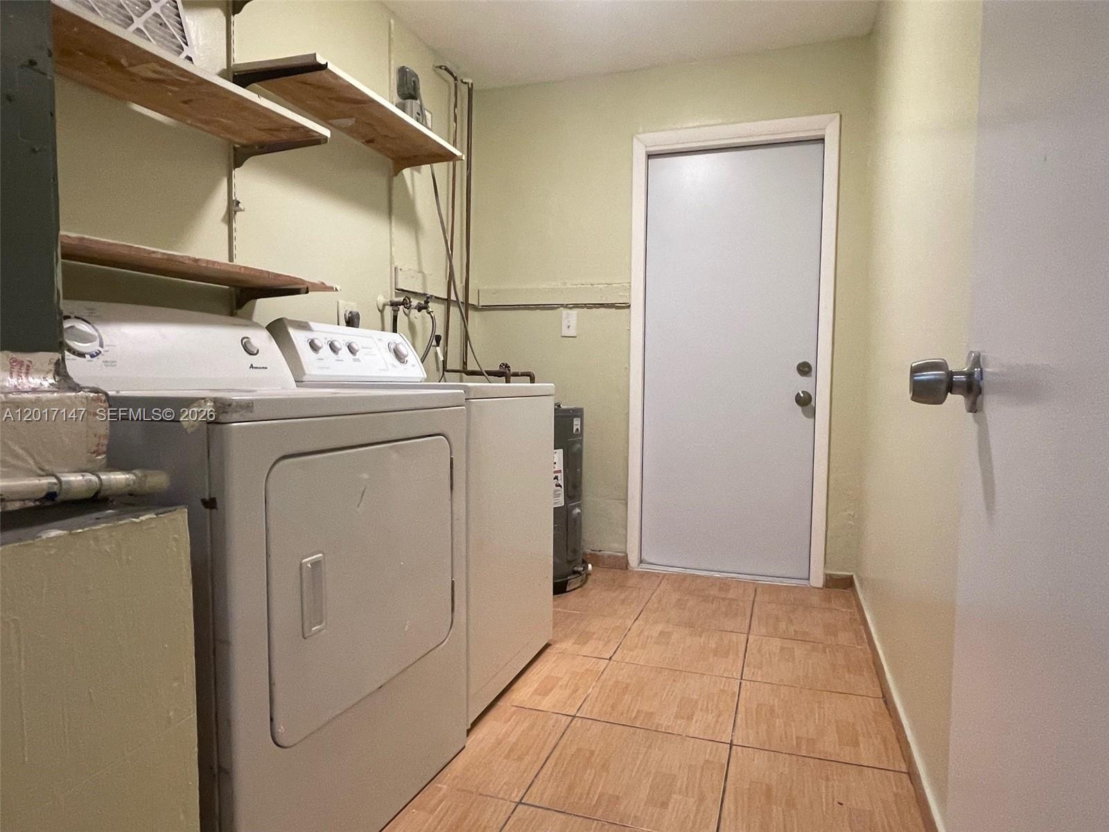 A laundry room features a washer, dryer, open shelving, and a door on tiled floors — 5960 NW 20th St # 5960, Lauderhill FL 33313, LAUDERHILL, FL