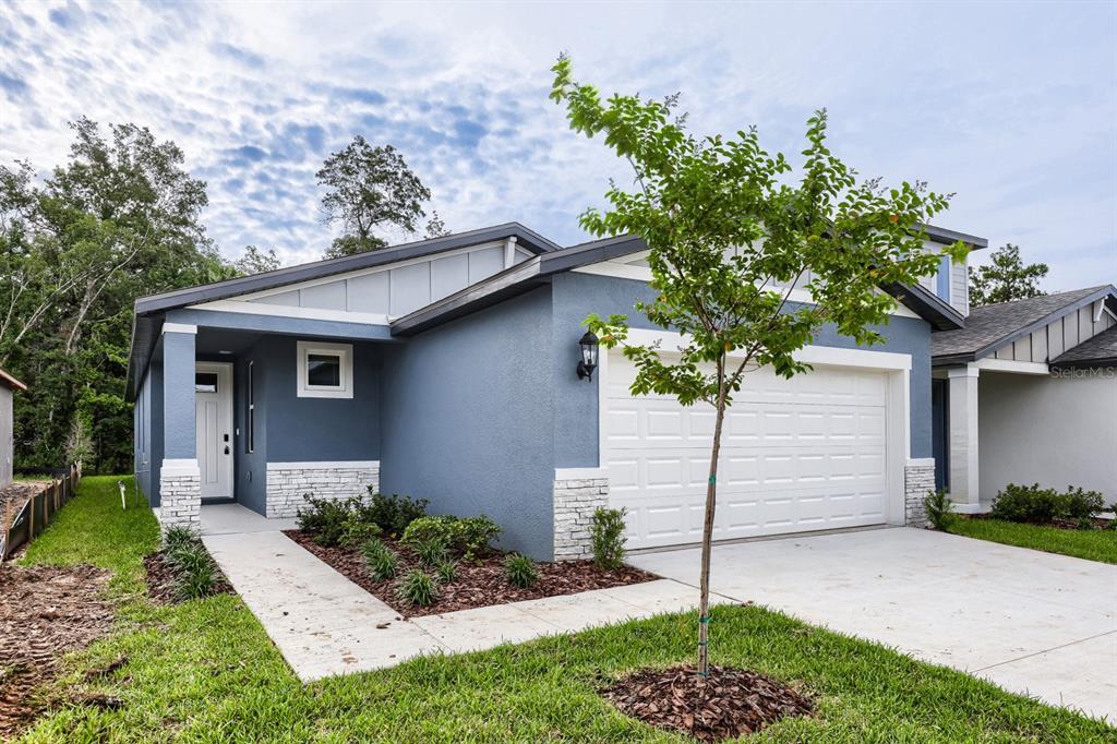 A blue single-story house with a white garage door, stone accents, and a front walkway — 7436 MIA VINE DRIVE, BROOKSVILLE, FL
