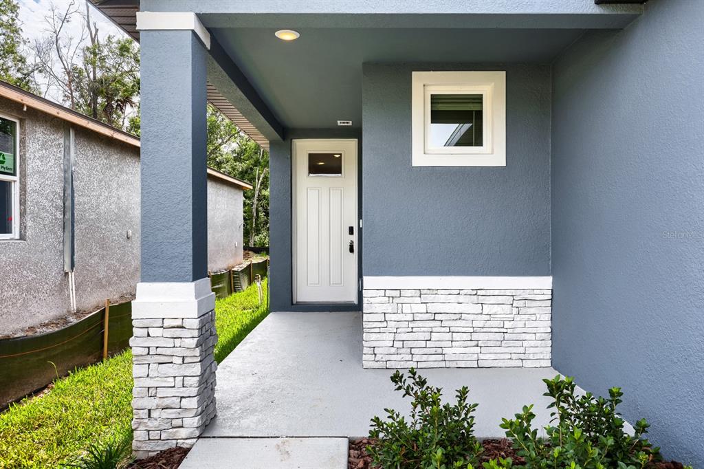 A covered front porch with a white door, stone accents, and a blue exterior wall — 7436 MIA VINE DRIVE, BROOKSVILLE, FL
