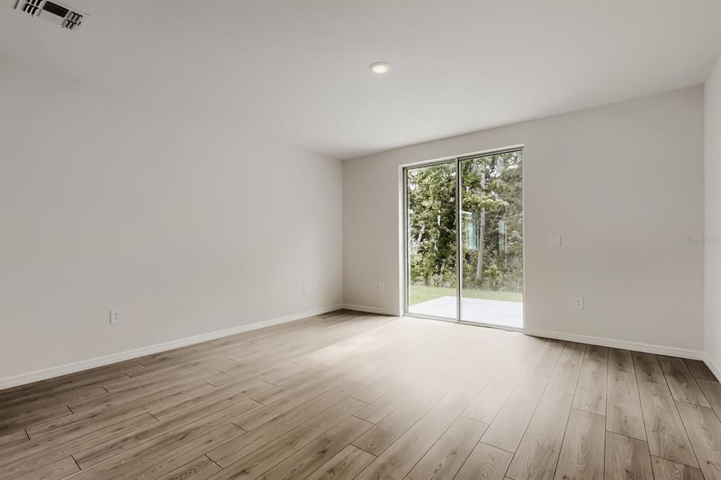 An empty room with light wood-look flooring, white walls, and a sliding glass door — 7436 MIA VINE DRIVE, BROOKSVILLE, FL