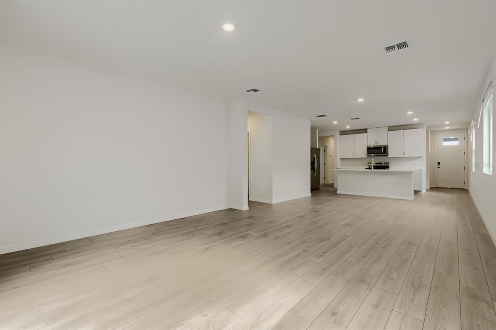 An open-concept living area features light wood-look flooring and a kitchen with white cabinetry — 7436 MIA VINE DRIVE, BROOKSVILLE, FL