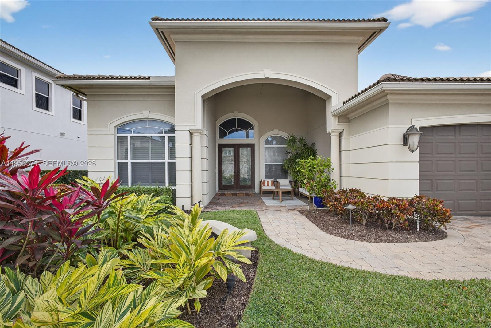 The exterior of a beige house features a covered entryway, arched windows, and a garage — 307 Charroux Dr, Palm Beach Gardens FL 33410, PALM BEACH GARDENS, FL