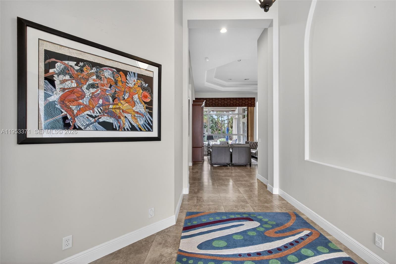 A hallway with tile floors, a large framed artwork, and a view into a living room — 307 Charroux Dr, Palm Beach Gardens FL 33410, PALM BEACH GARDENS, FL