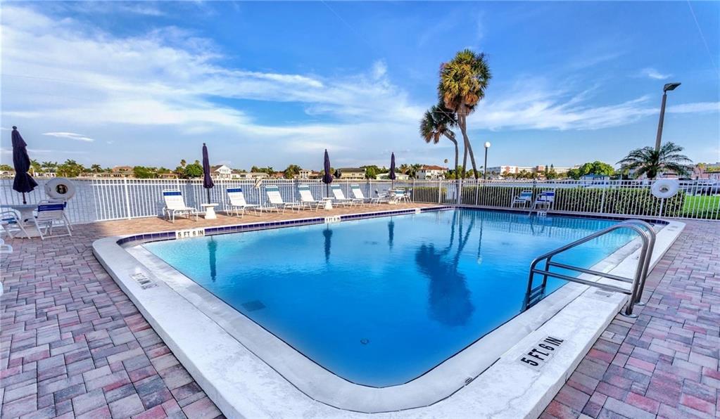 Two tall apartment buildings stand behind a covered parking structure in a paved lot — 400 64TH AVENUE UNIT 405, ST PETE BEACH, FL