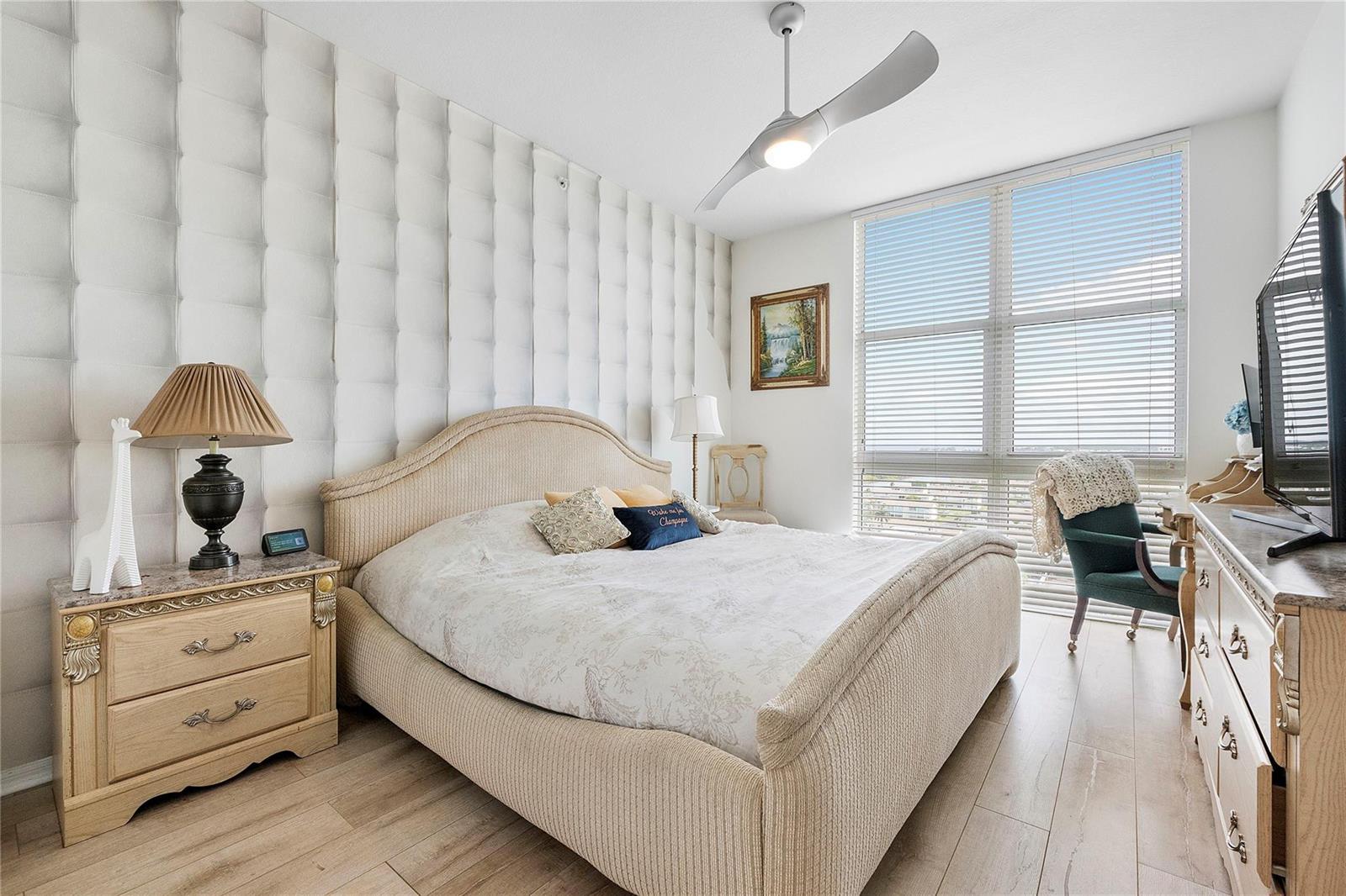 A bedroom features a tufted white accent wall, a beige upholstered bed, and a ceiling fan — 625 Casa Loma Boulevard # 1608, Boynton Beach FL 33435, BOYNTON BEACH, FL