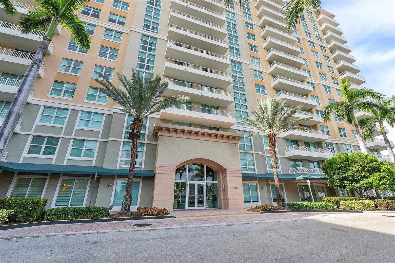 The exterior of a multi-story apartment building features balconies, palm trees, and a central entrance — 625 Casa Loma Boulevard # 1608, Boynton Beach FL 33435, BOYNTON BEACH, FL