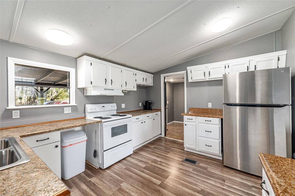 A kitchen with white cabinets, granite countertops, stainless steel appliances, and wood-look flooring — 5600 SE 39TH STREET, TRENTON, FL