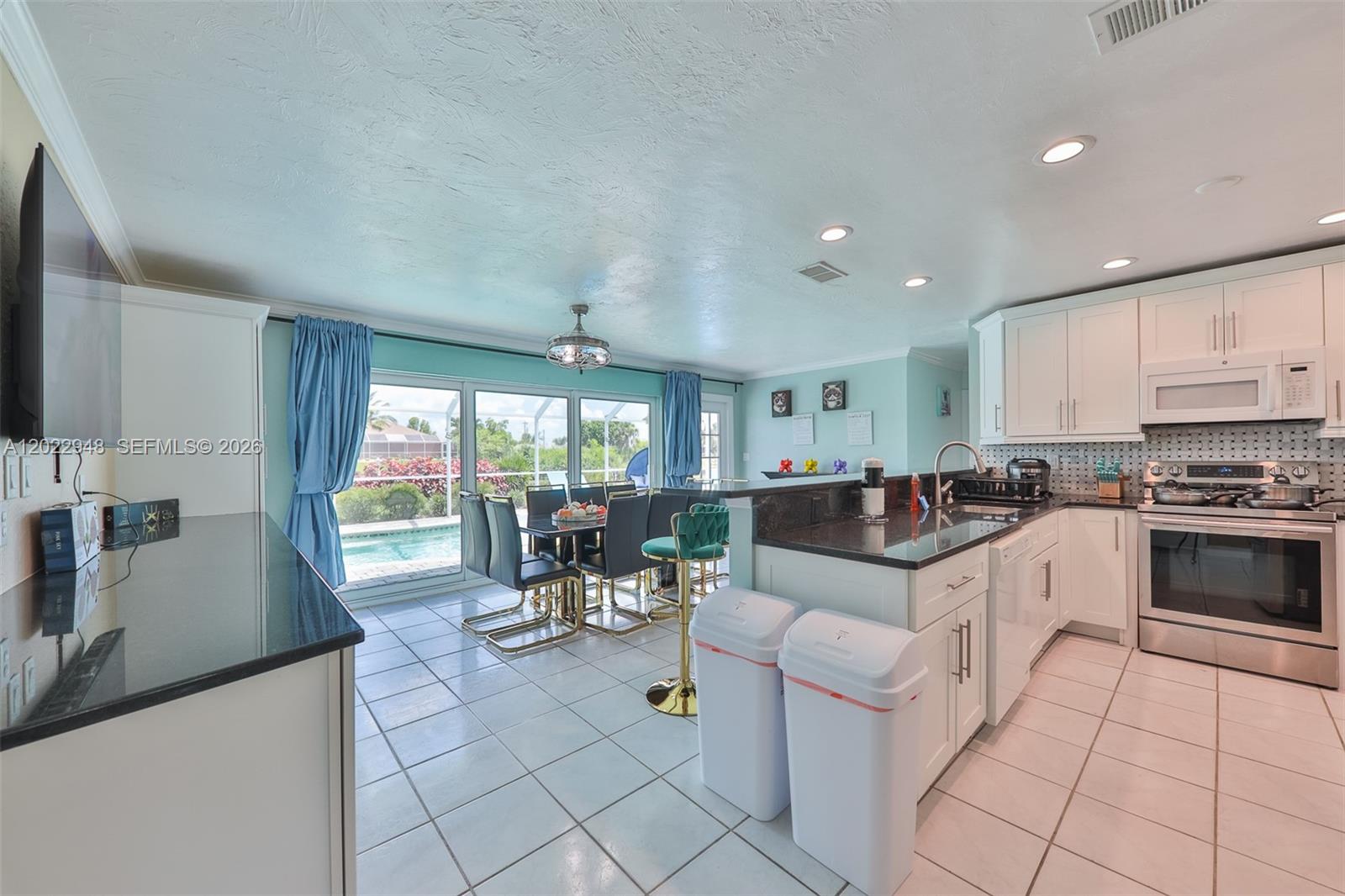 A kitchen and dining area features white cabinets, dark countertops, tile floors, and pool views — 503 SW 17 St, Cape Coral FL 33990, CAPE CORAL, FL