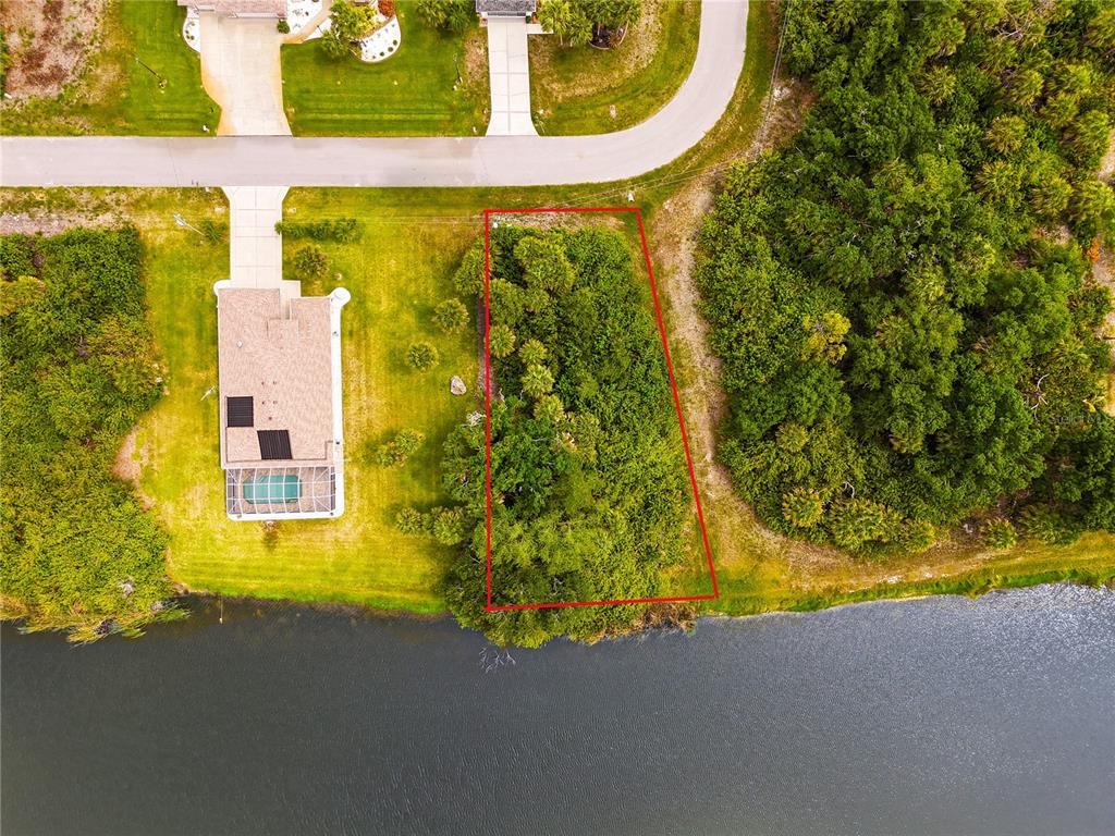 An aerial view shows a vacant, wooded residential lot outlined in red next to a lake — 123 GARLAND WAY, ROTONDA WEST, FL