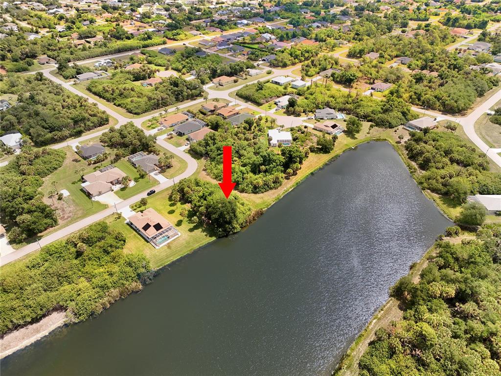 An aerial view shows a vacant, wooded lot situated along a lake in a neighborhood — 123 GARLAND WAY, ROTONDA WEST, FL