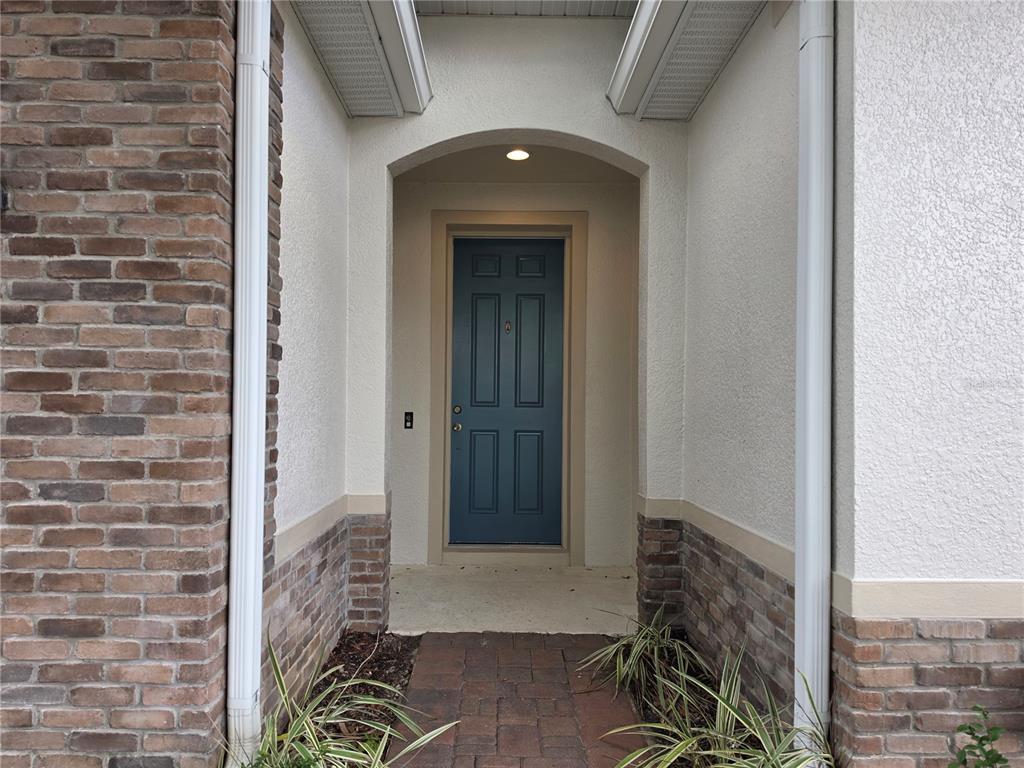 A blue front door is recessed within a covered entryway featuring brick accents and stucco — 549 BETHESDA COURT, OVIEDO, FL