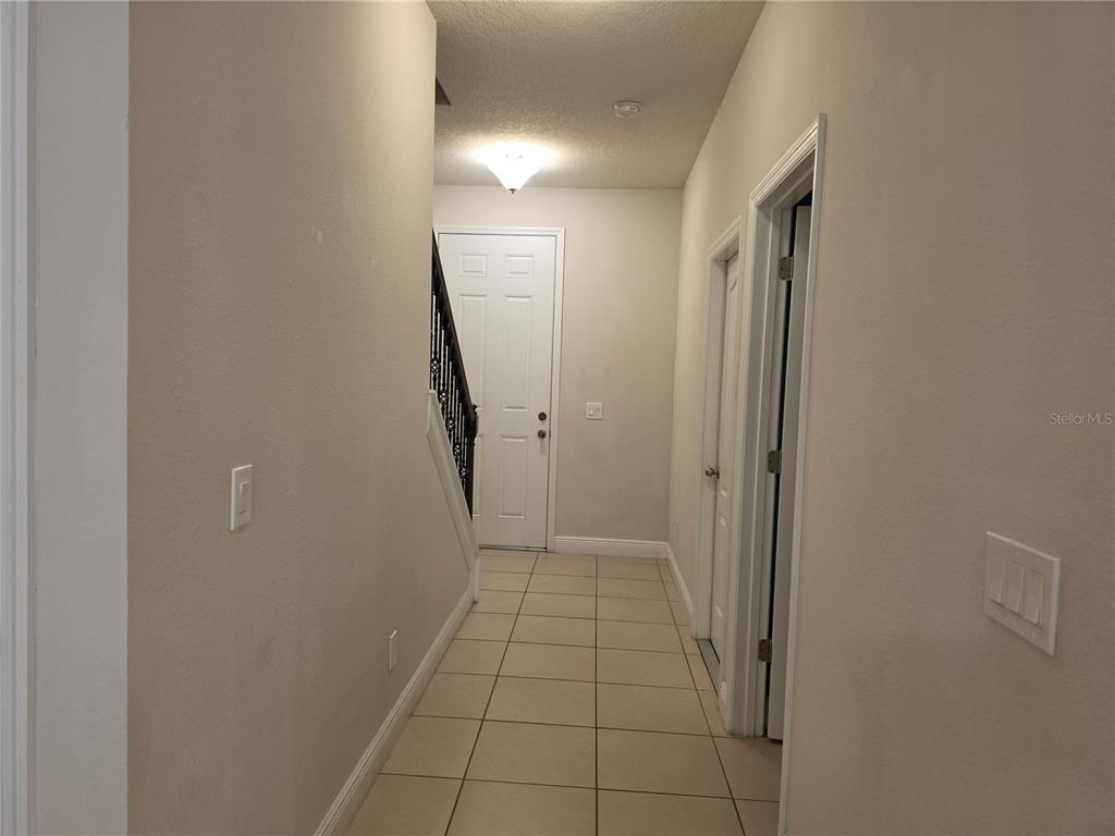 A tiled hallway features a staircase with a dark railing and a white front door — 549 BETHESDA COURT, OVIEDO, FL