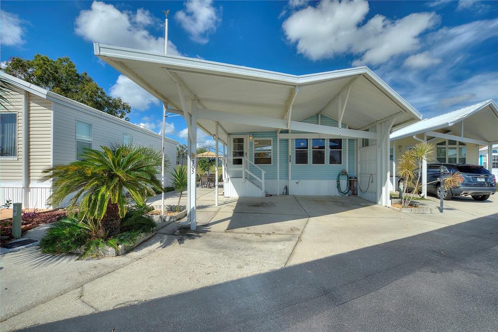 A light blue mobile home features a large attached carport and a concrete driveway — 305 ARNOLD PALMER DRIVE, DAVENPORT, FL