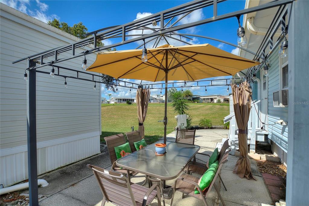 A patio features a metal pergola with string lights, a dining set, and a yellow umbrella — 305 ARNOLD PALMER DRIVE, DAVENPORT, FL