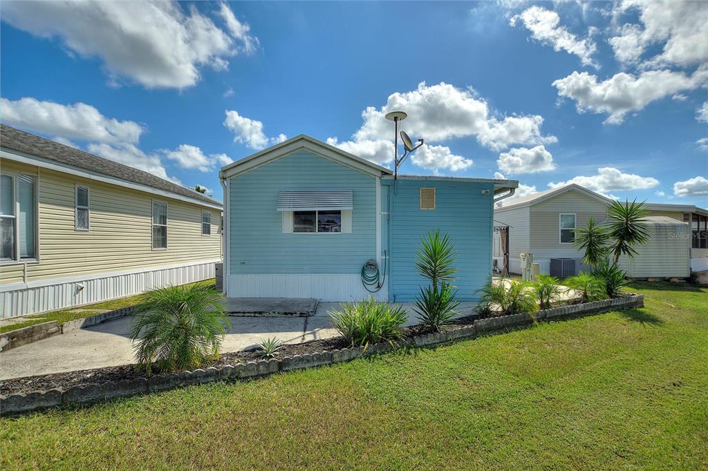 The exterior of a light blue mobile home features a concrete patio and landscaping — 305 ARNOLD PALMER DRIVE, DAVENPORT, FL