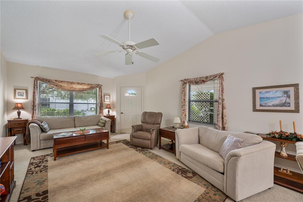 A living room with a vaulted ceiling, ceiling fan, carpeted floors, and an adjacent dining area — 4918 PLEASANT HOLLOW TRAIL, LAKELAND, FL