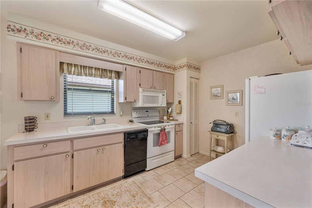 A kitchen with light wood cabinets, white appliances, and tile flooring opens to a dining area — 4918 PLEASANT HOLLOW TRAIL, LAKELAND, FL
