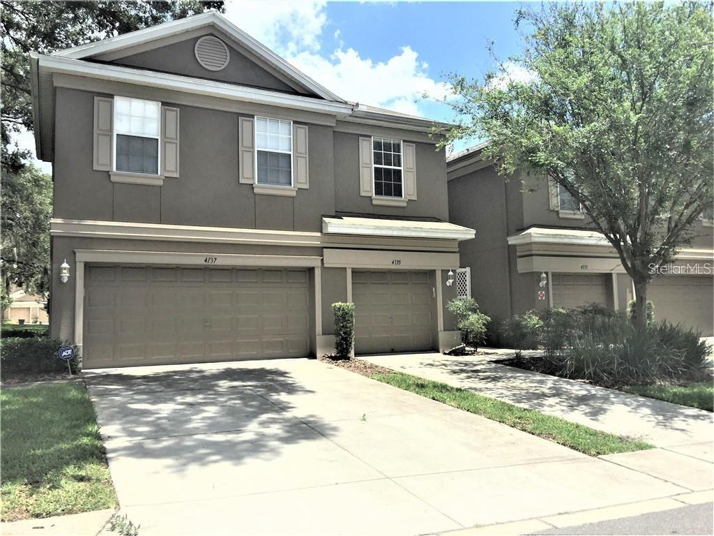 A two-story townhouse exterior features two garage doors, beige siding, and a concrete driveway — 4135 BISMARCK PALM DRIVE, TAMPA, FL