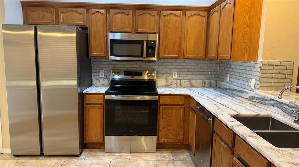 A kitchen features wood cabinets, stainless steel appliances, and marble-patterned countertops with a subway tile backsplash — 4135 BISMARCK PALM DRIVE, TAMPA, FL
