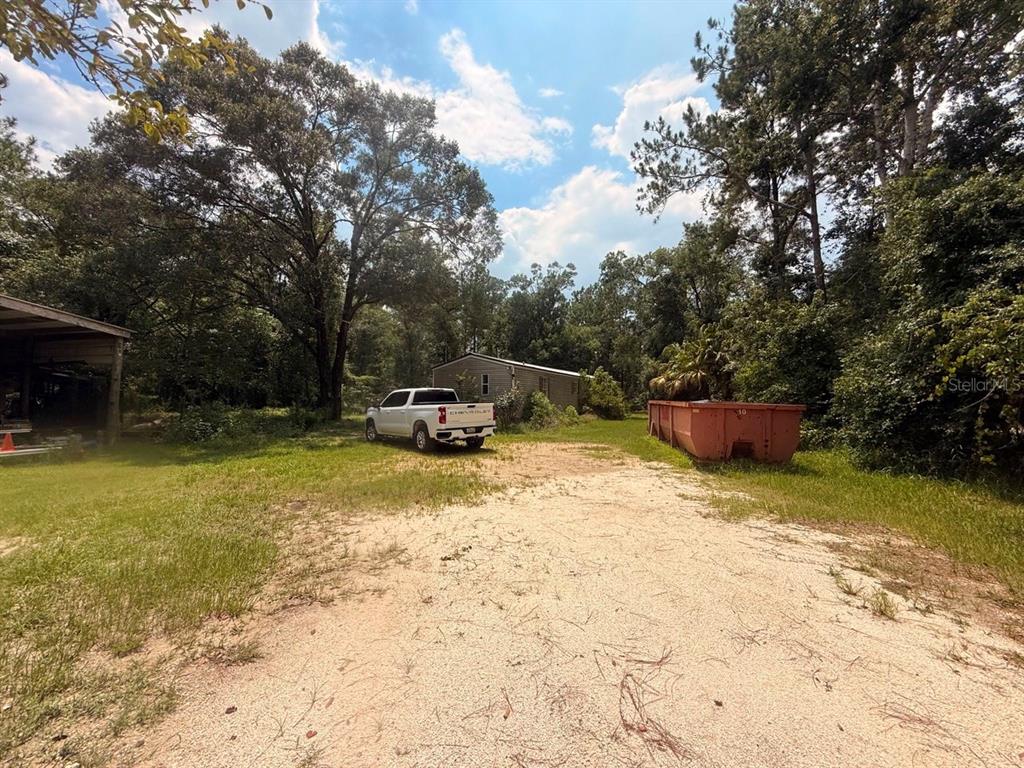 A white pickup truck and a large dumpster sit on a dirt lot near trees — 10105 MCMAHON AVENUE, HASTINGS, FL