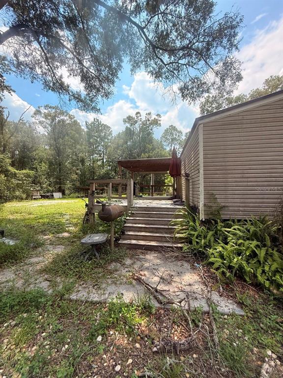 A wooden deck with stairs leads to a house exterior surrounded by trees and vegetation — 10105 MCMAHON AVENUE, HASTINGS, FL