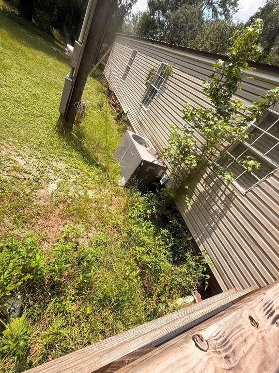 An exterior view of a mobile home with beige siding, an HVAC unit, and overgrown vegetation — 10105 MCMAHON AVENUE, HASTINGS, FL