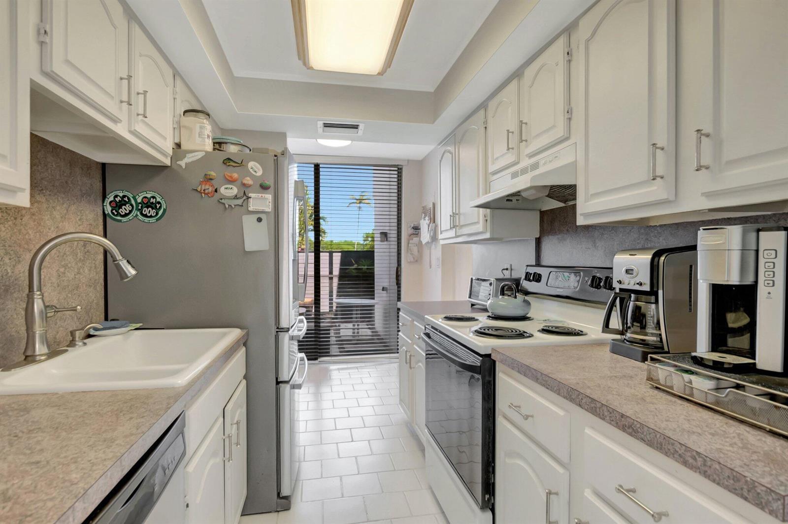 A galley kitchen features white cabinets, gray countertops, stainless steel appliances, and a sliding glass door — 3705 Bridgewood Drive, Boca Raton FL 33434, BOCA RATON, FL