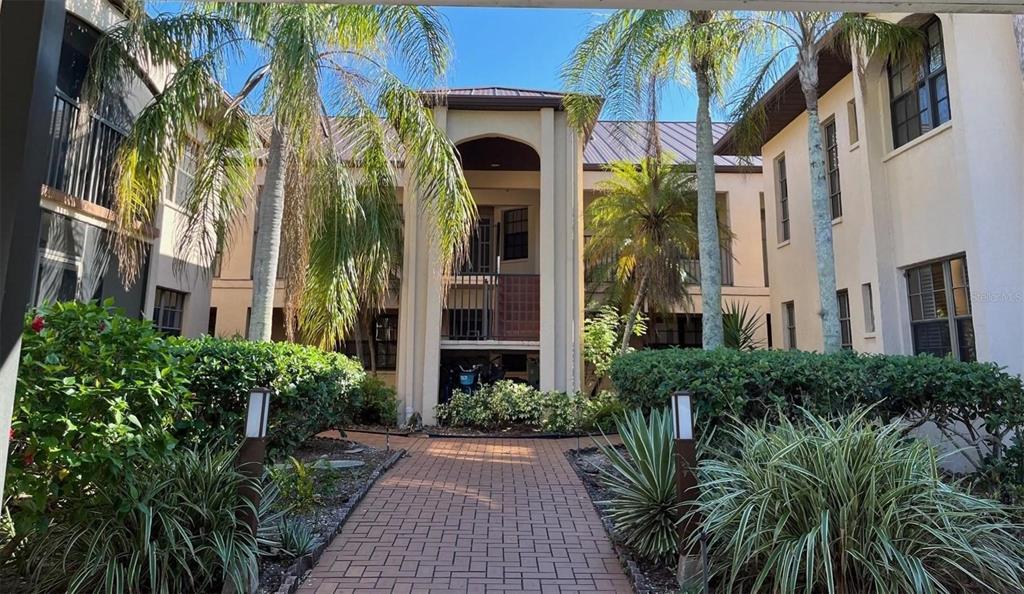 A brick walkway leads to the entrance of a multi-story apartment building with palm trees — 23465 HARBORVIEW ROAD UNIT 1006, PUNTA GORDA, FL