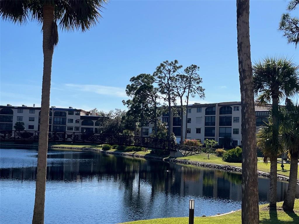 A pedestrian bridge crosses a pond in front of multi-story apartment buildings — 23465 HARBORVIEW ROAD UNIT 1006, PUNTA GORDA, FL