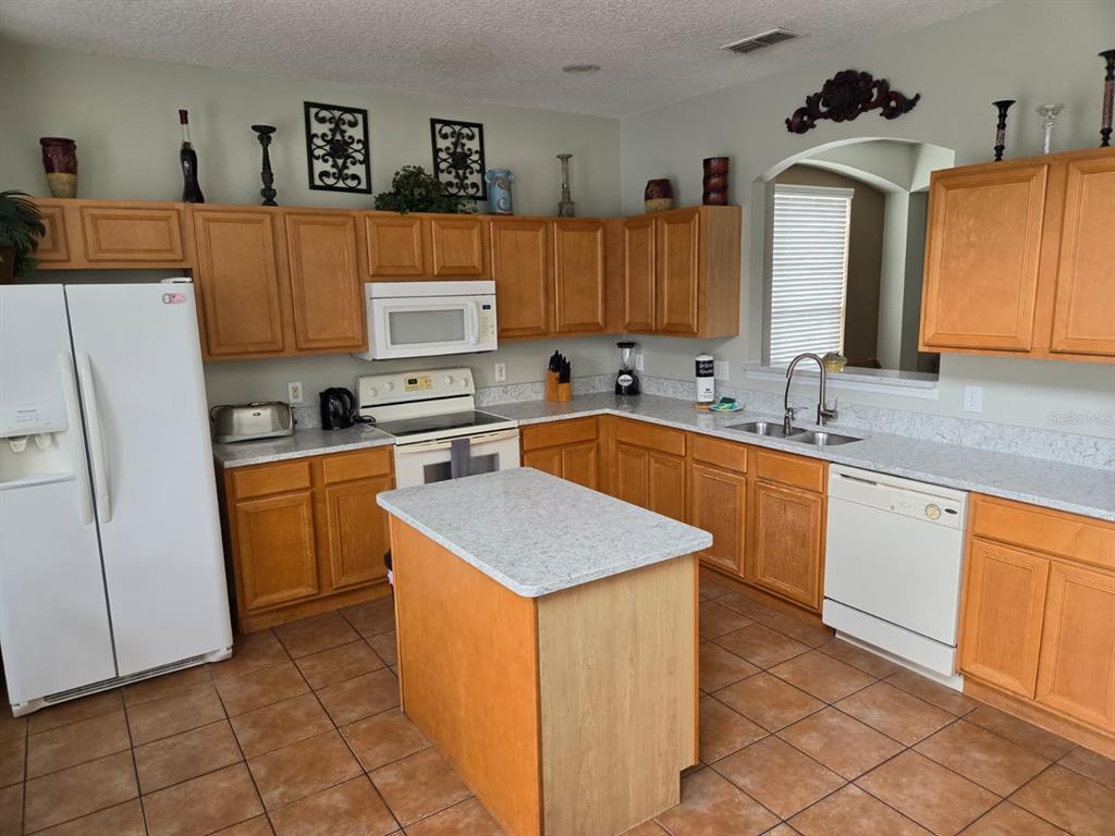 A kitchen features light wood cabinets, speckled countertops, a central island, and white appliances — 256 SEVILLA AVENUE, DAVENPORT, FL
