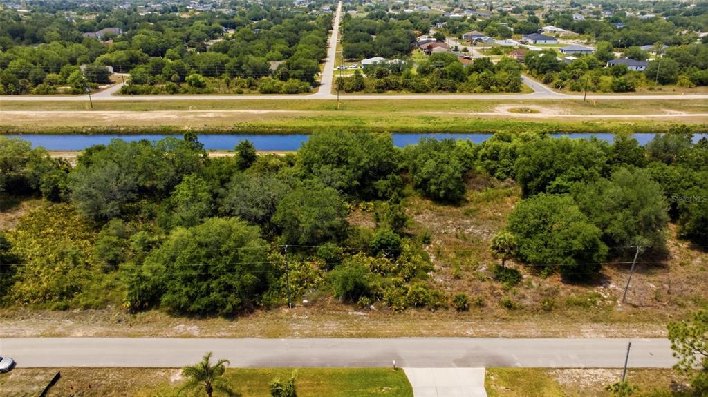 An aerial view shows a vacant, tree-covered lot situated between a road and a canal — 1909 WESTBORO LOOP, LEHIGH ACRES, FL