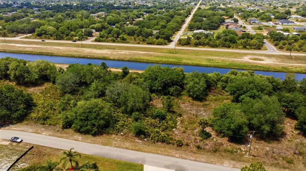 An aerial view shows a vacant, wooded lot situated between a road and a canal — 1909 WESTBORO LOOP, LEHIGH ACRES, FL