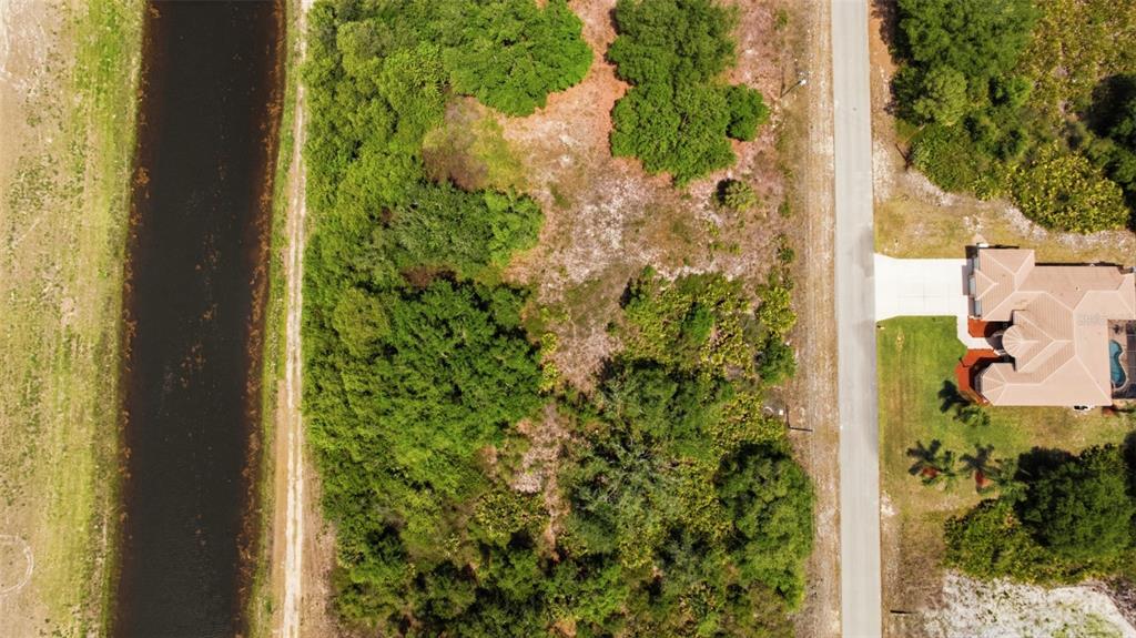 An aerial view shows a vacant wooded lot next to a road and a house — 1909 WESTBORO LOOP, LEHIGH ACRES, FL