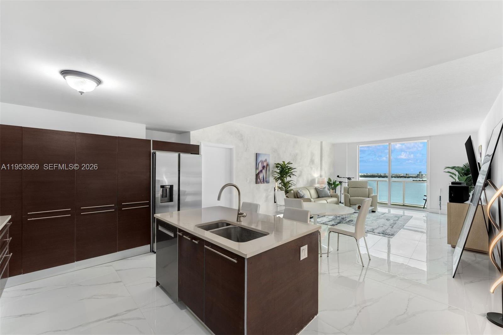 A modern kitchen with dark wood cabinetry and a central island overlooks a bright living area — 1900 N Bayshore Dr # 3202, Miami FL 33132, MIAMI, FL