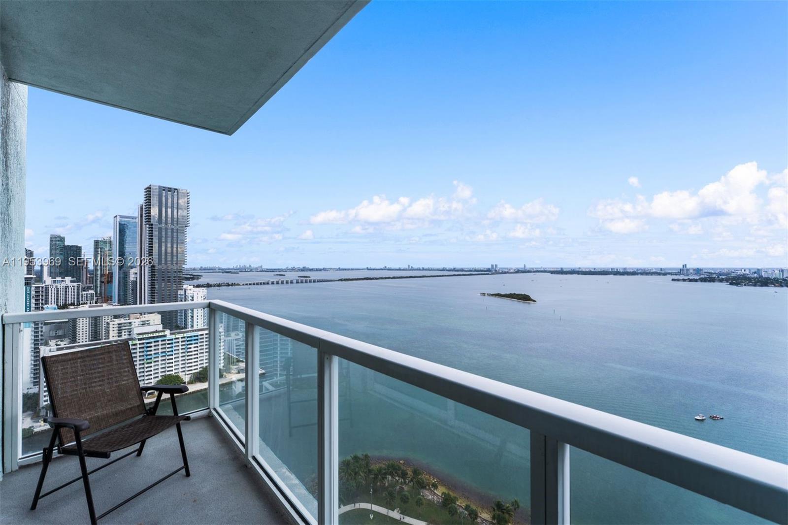 A balcony with a chair overlooks a large body of water and a city skyline — 1900 N Bayshore Dr # 3202, Miami FL 33132, MIAMI, FL