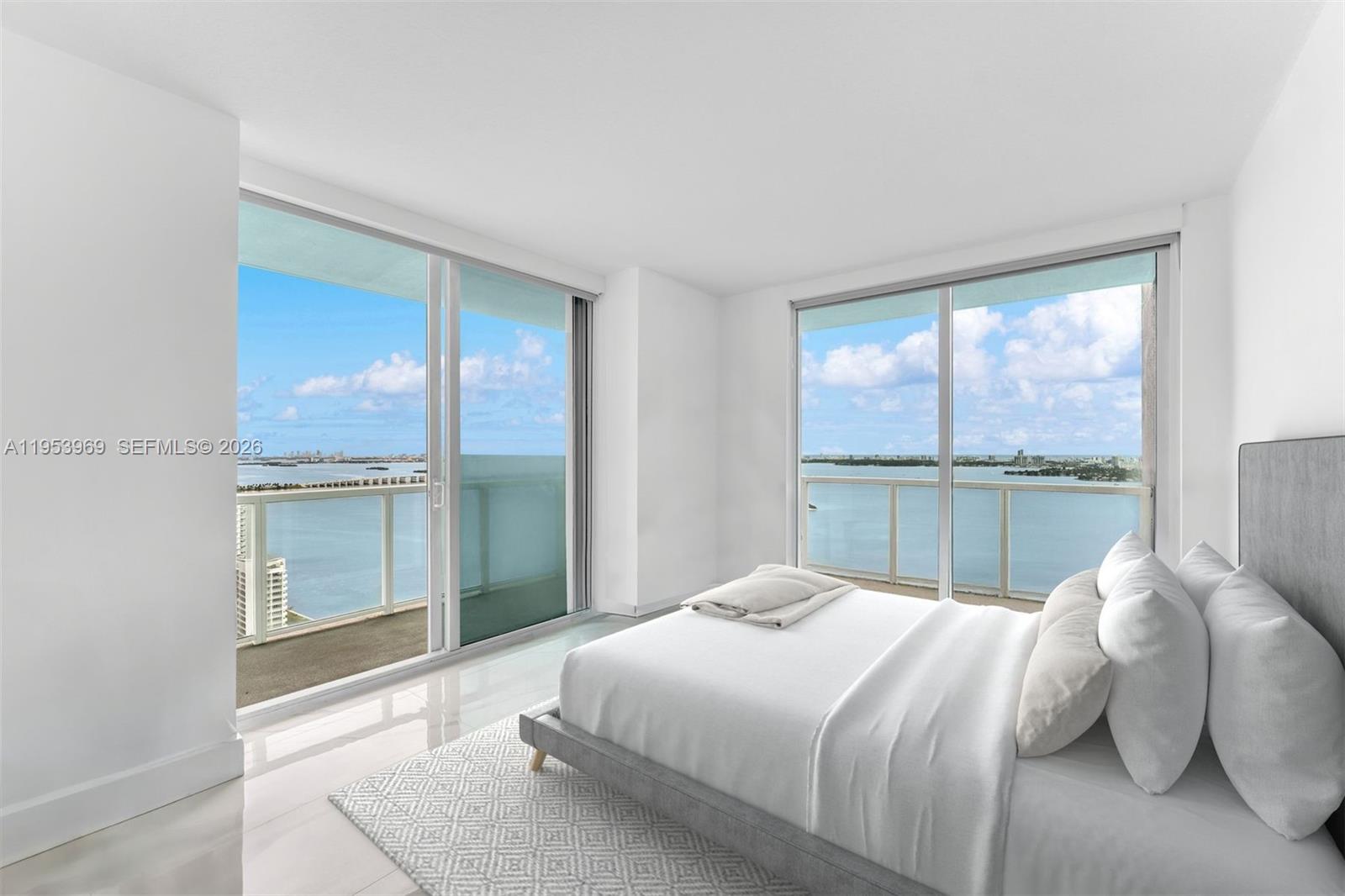 A modern bedroom features white walls, tile floors, and floor-to-ceiling windows overlooking the water — 1900 N Bayshore Dr # 3202, Miami FL 33132, MIAMI, FL