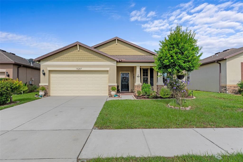 A single-story suburban house with a tan exterior, two-car garage, and a front lawn — 15287 STONE HOUSE DRIVE, BROOKSVILLE, FL