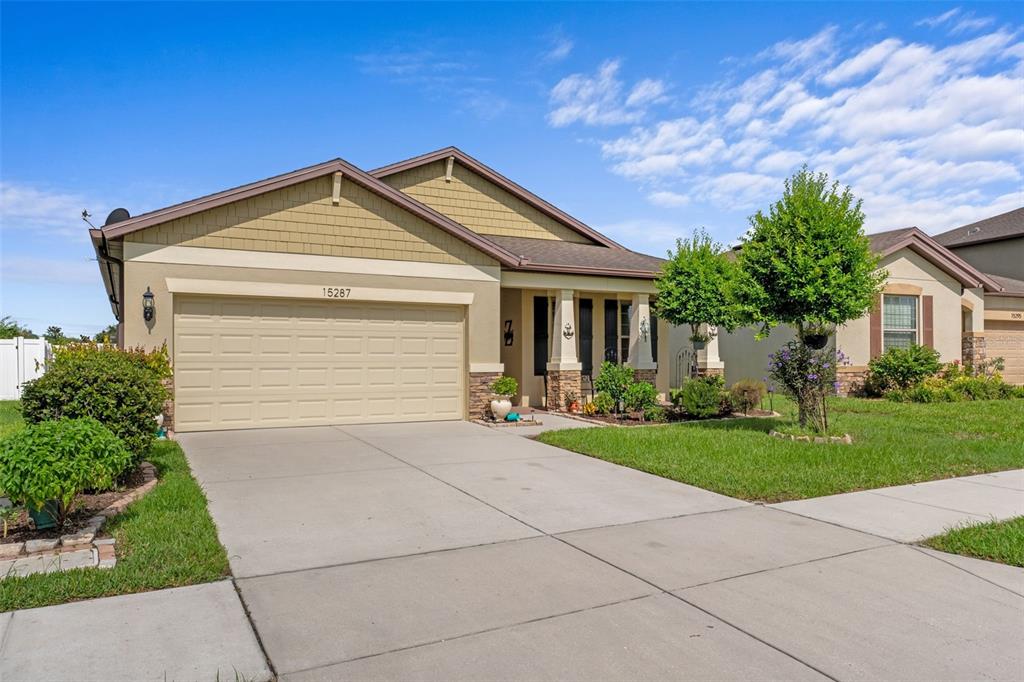 A single-story suburban house features a two-car garage, tan siding, and a covered front porch — 15287 STONE HOUSE DRIVE, BROOKSVILLE, FL