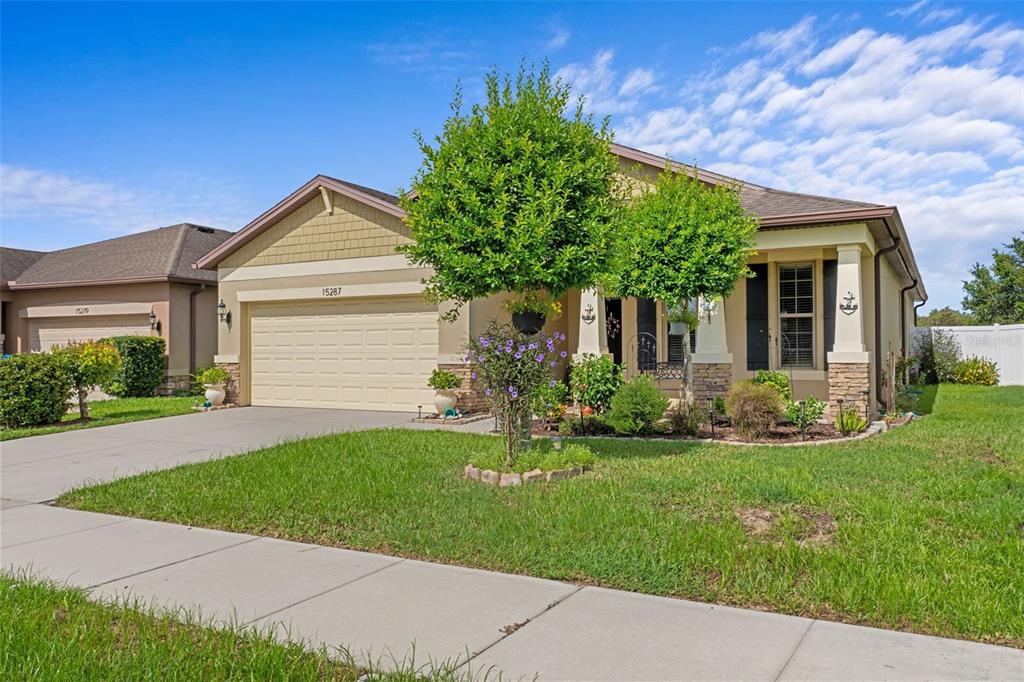 A single-story suburban house with a tan facade, a two-car garage, and a front lawn — 15287 STONE HOUSE DRIVE, BROOKSVILLE, FL