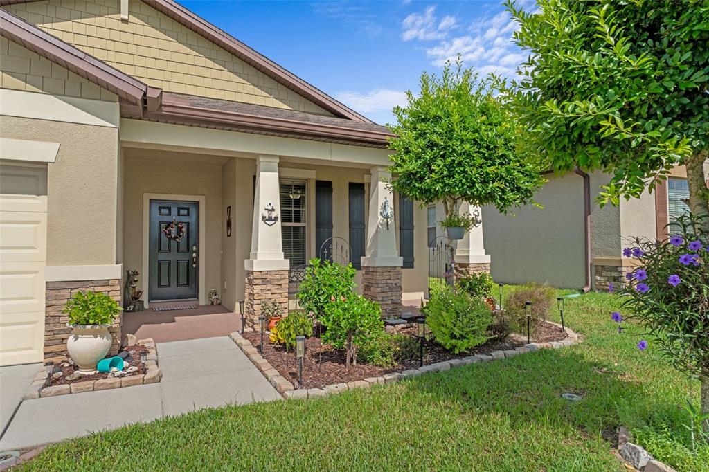 A suburban home exterior features a covered porch, stone-based columns, and a landscaped front yard — 15287 STONE HOUSE DRIVE, BROOKSVILLE, FL