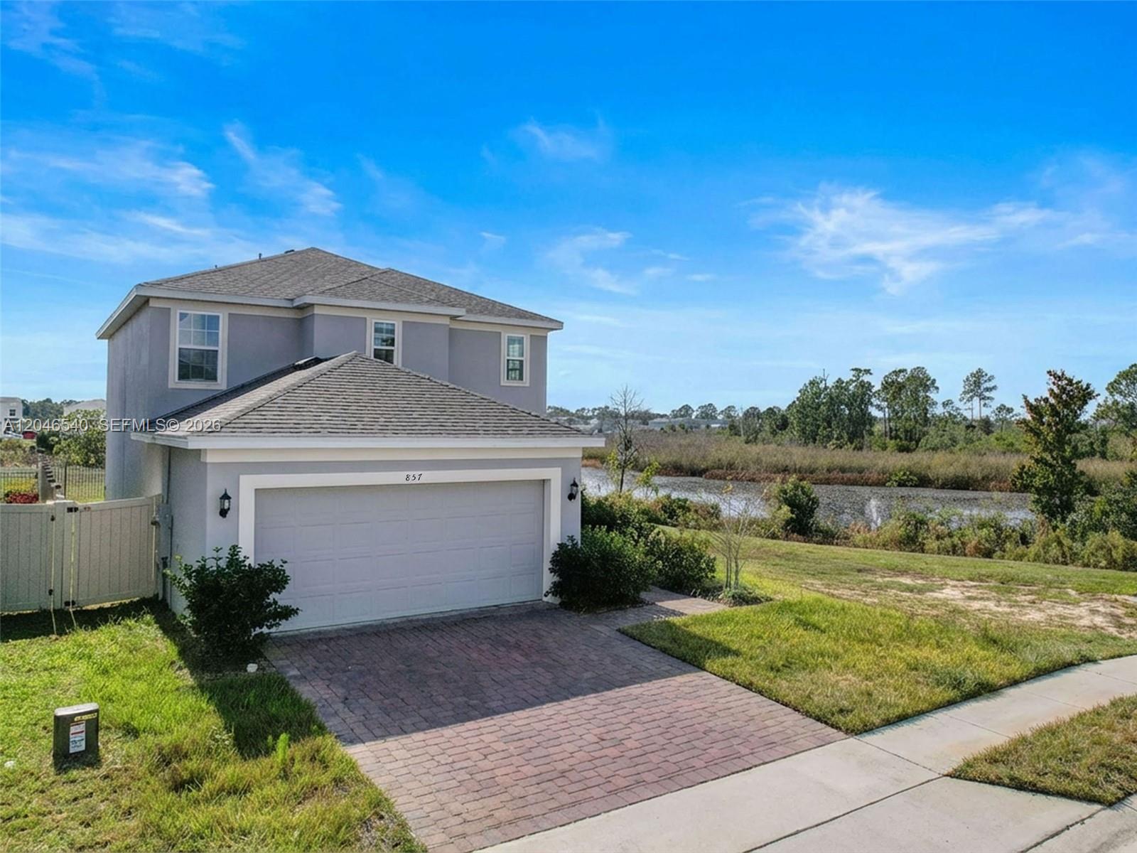 A two-story gray house with a brick driveway sits next to a small pond — 857 scrub oak hammock rd, Davenport FL 33837, DAVENPORT, FL