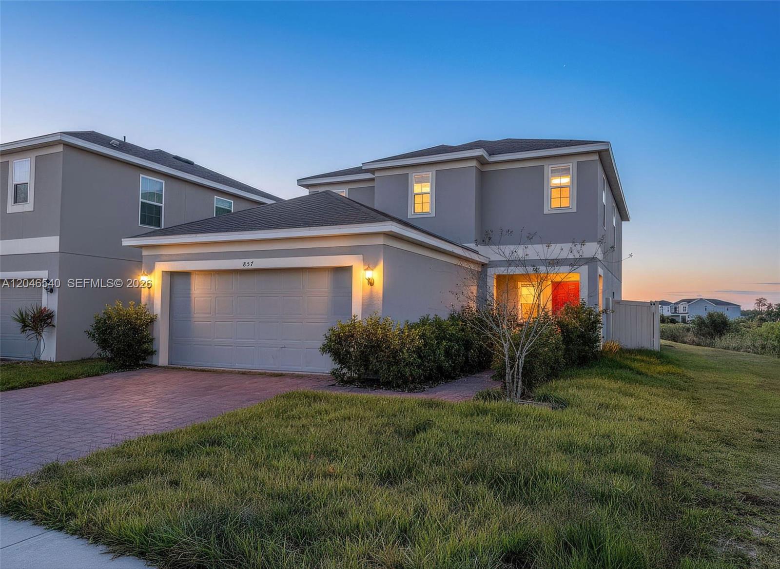 A two-story gray house with a two-car garage and a paved driveway at dusk — 857 scrub oak hammock rd, Davenport FL 33837, DAVENPORT, FL